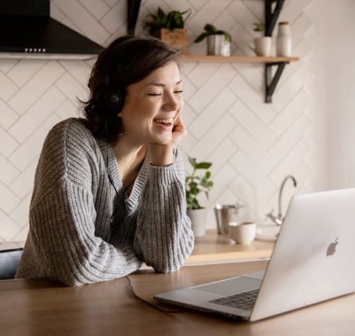 A woman who is sitting at a table with an Apple Macbook Pro in front of her. She is video calling with someone.